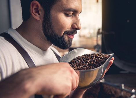 Man Smelling and Holding Metal Scoop Full of Coffee Beans in Hands