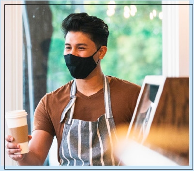 Male Barista With a Mask on Holding a Coffee Cup in Hand Male Barista With a Mask on Holding a Coffee Cup in Hand