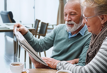 Man & Woman Reading Newspaper Enjoying Coffee in Senior Living Facility Man & Woman Reading Newspaper Enjoying Coffee in Senior Living Facility