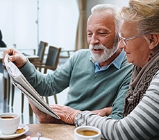 Man & Woman Reading Newspaper Enjoying Coffee in Senior Living Facility Man & Woman Reading Newspaper Enjoying Coffee in Senior Living Facility