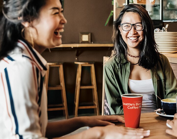Women Sitting at a Table Enjoying Seattle’s Best Coffee Cup Women Sitting at a Table Enjoying Seattle’s Best Coffee Cup