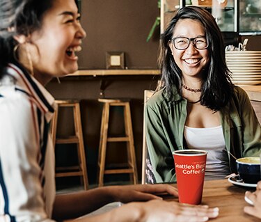 Women Sitting at a Table Enjoying Seattle’s Best Coffee Cup Women Sitting at a Table Enjoying Seattle’s Best Coffee Cup